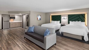 A hotel room with a sofa, two beds, a kitchenette, and a modern design.