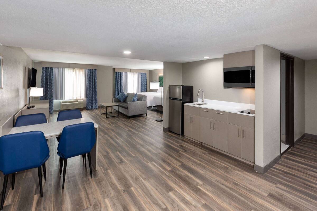 A modern hotel room with a dining area, kitchenette, and a living space.