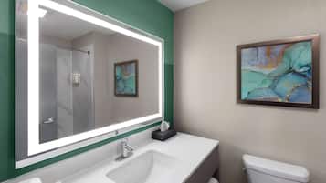 Une salle de bain avec un grand miroir, un lavabo, des toilettes et un tableau abstrait encadré accroché au mur.
