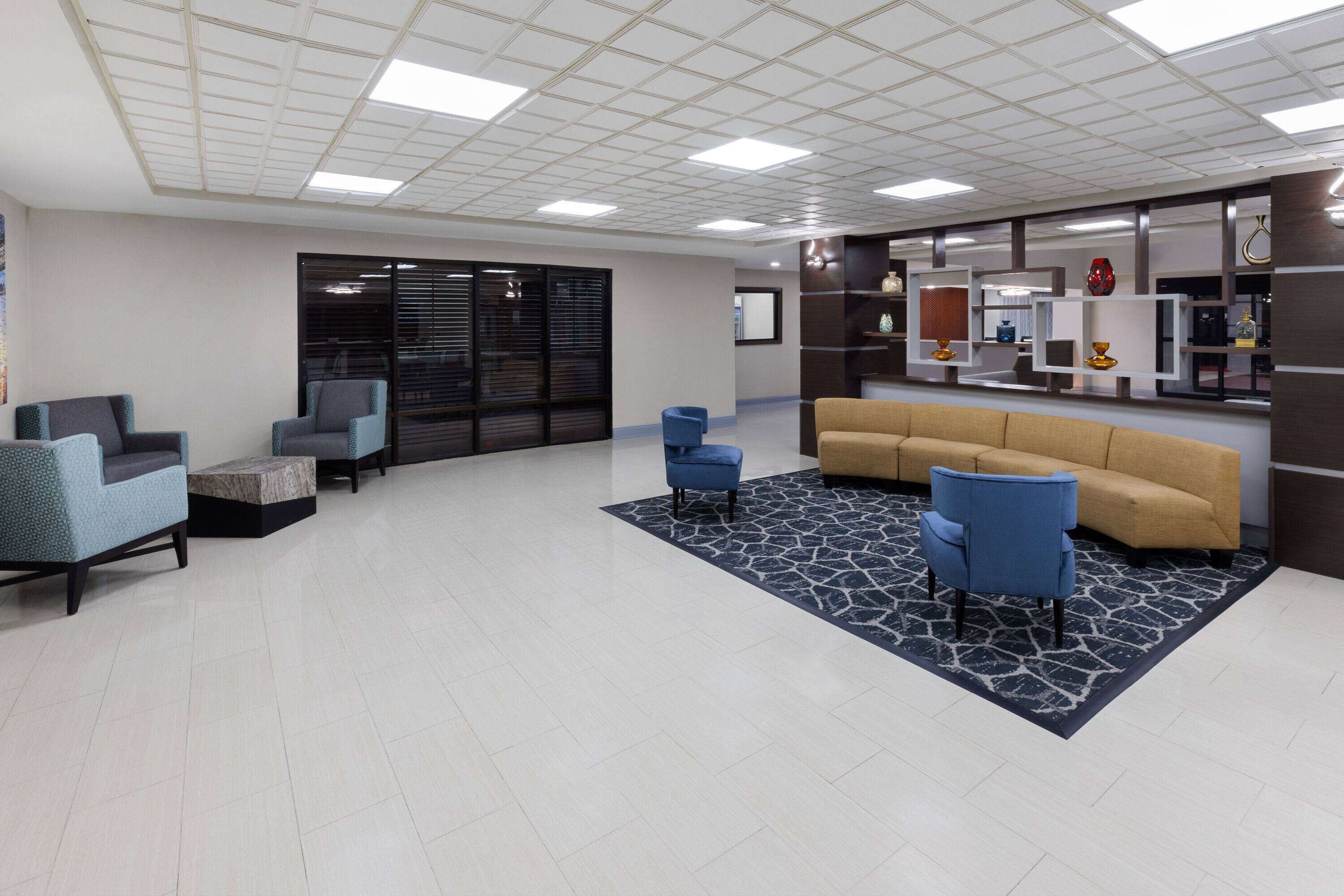 A spacious lobby with a beige sofa, blue armchairs, and a patterned rug.