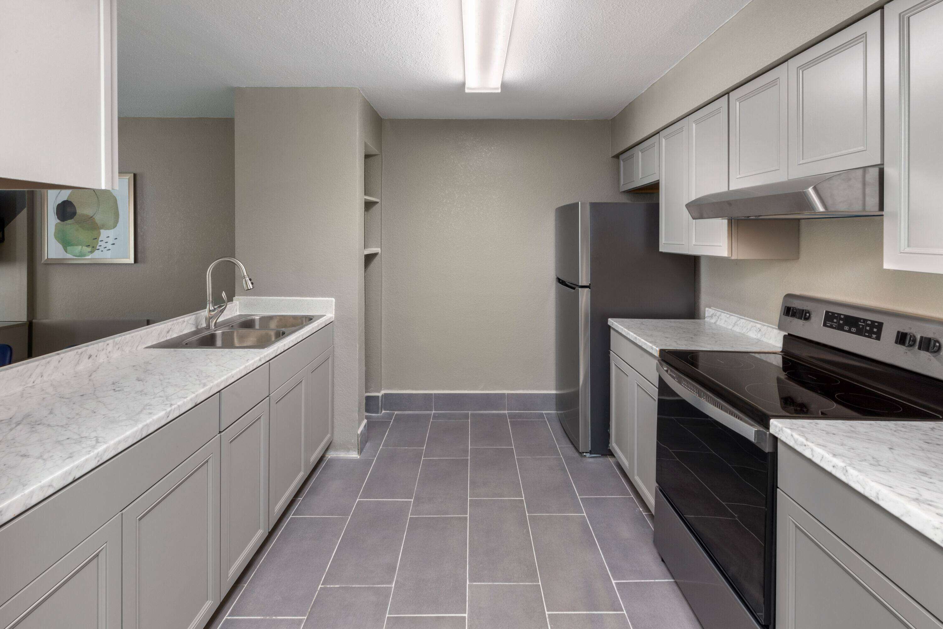 A modern kitchen with grey cabinets, a stainless steel refrigerator, a black oven, and a marble countertop.