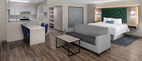 Quarto de hotel moderno com cozinha compacta, sofá, cama e escrivaninha.