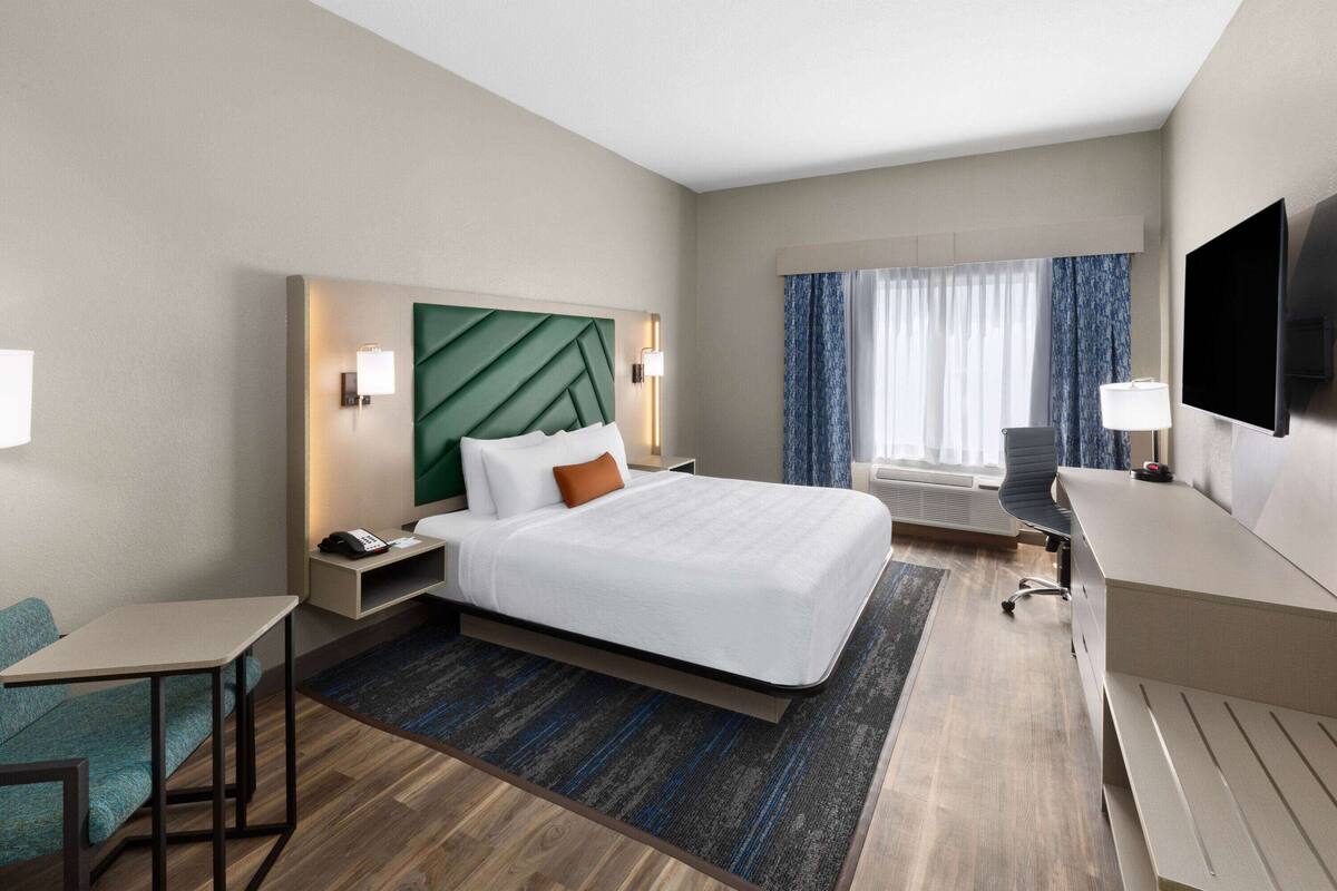A modern hotel room with a large bed, a desk, a chair, a TV, and a window with curtains.