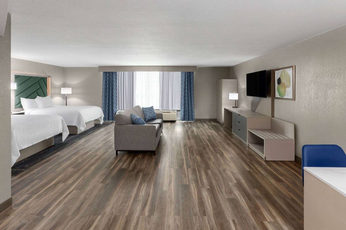 A hotel room with a large bed, a sofa, a desk, and a TV.