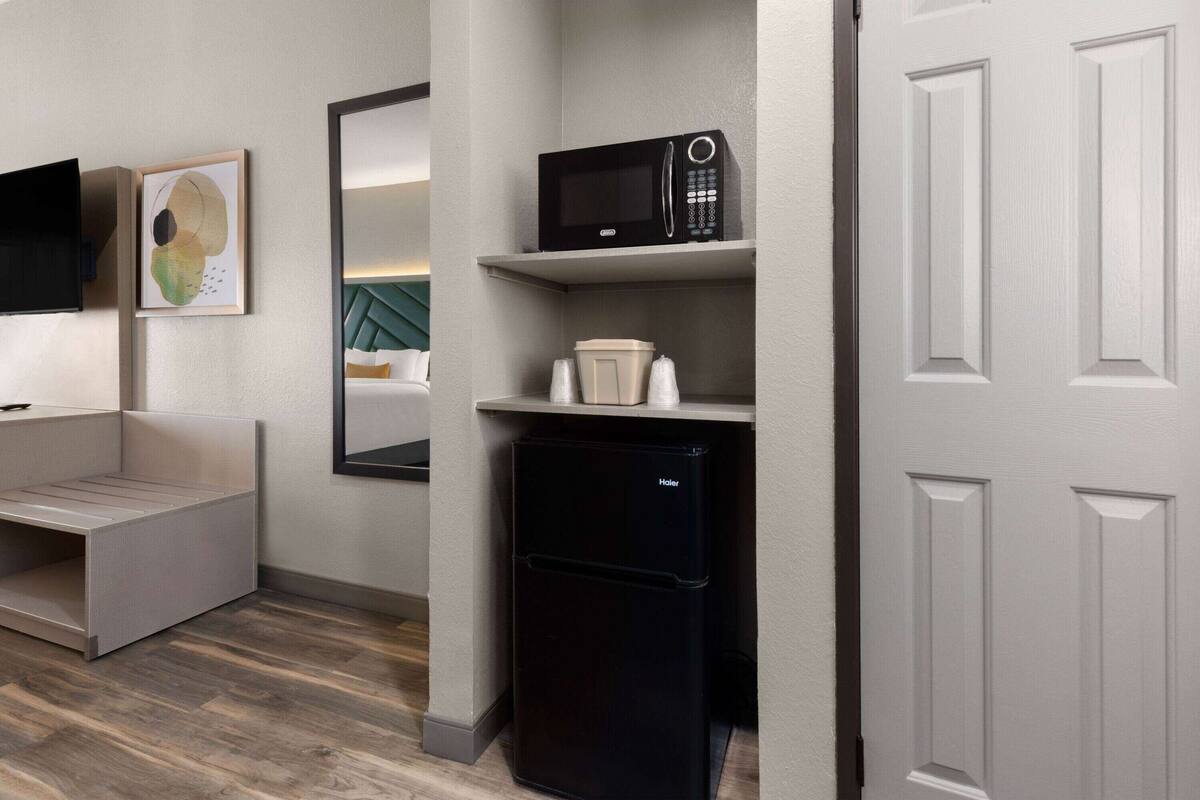 A compact kitchenette with a black refrigerator, a microwave, and a small coffee maker on a shelf.