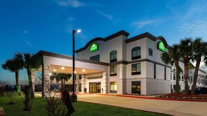 A modern hotel with a two-story structure, a covered entrance, and a landscaped front yard with palm trees.