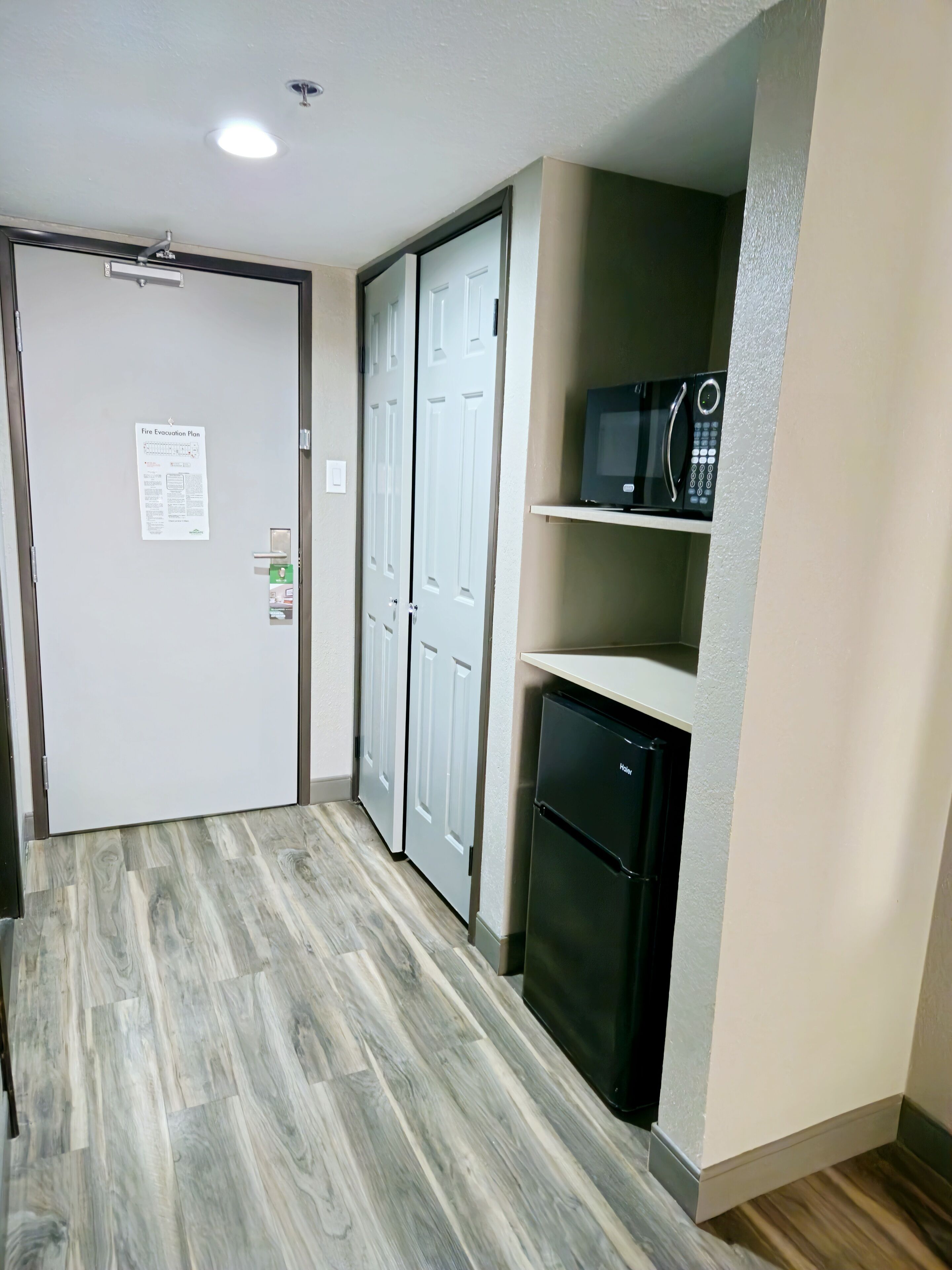 A compact kitchen with a built-in microwave, a mini refrigerator, and a door with a fire evacuation plan.