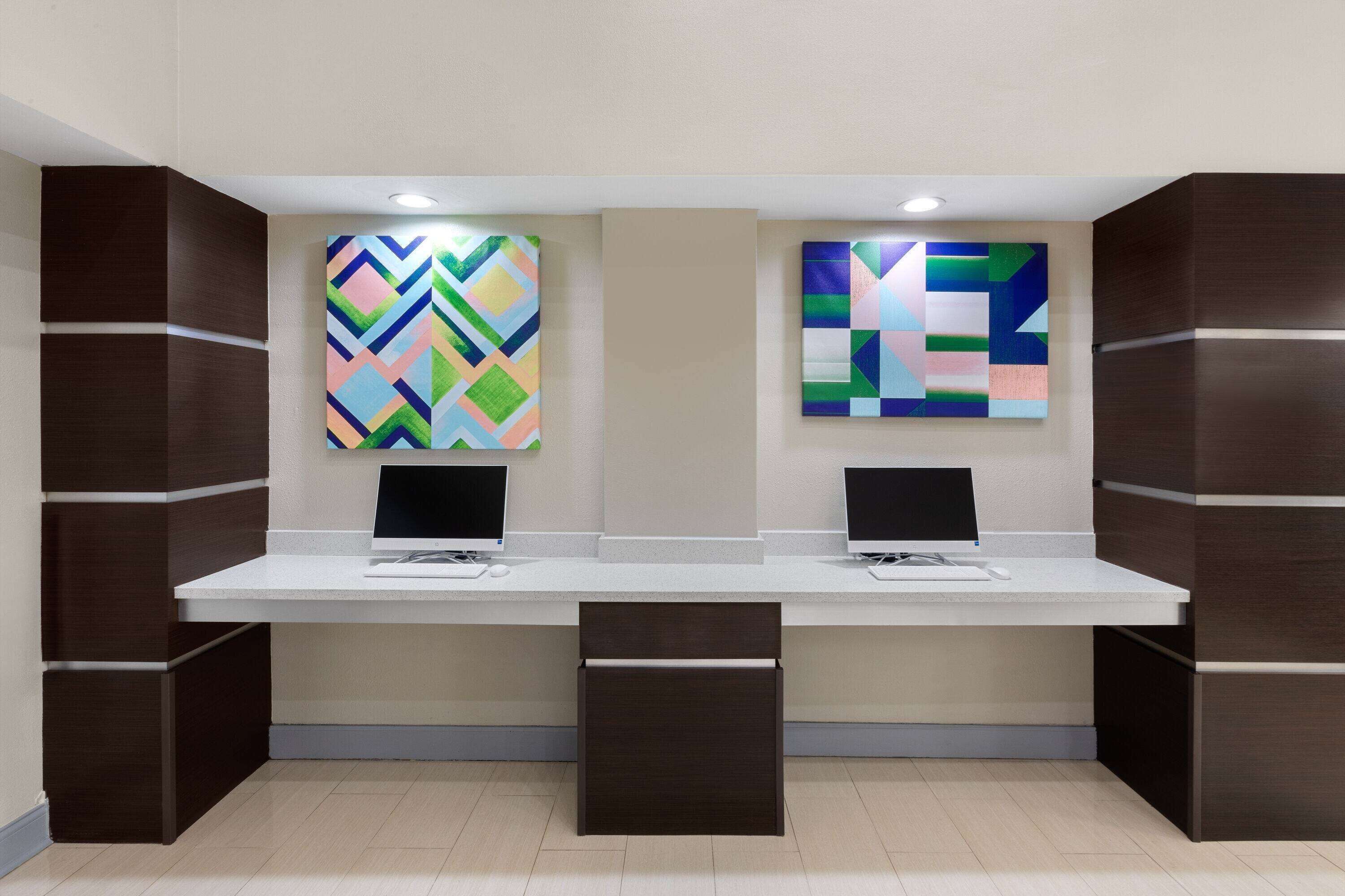 A reception desk with two computer monitors, a white counter, and two abstract paintings on the wall.