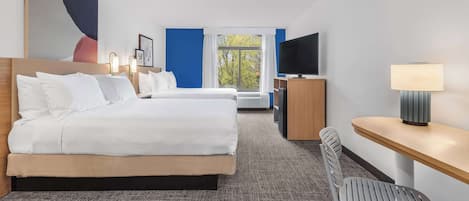 A hotel room with a large bed, a desk, a chair, a TV, and a window with a view of trees.