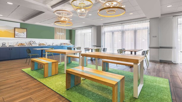A modern dining area with wooden tables and benches, a bar area, and large windows with curtains. - Spark by Hilton Charlotte Tyvola I-77 (Charlotte)