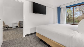 Quarto de hotel moderno com uma cama grande, televisão de tela plana na parede, uma mesa pequena e vista para o exterior pela janela.