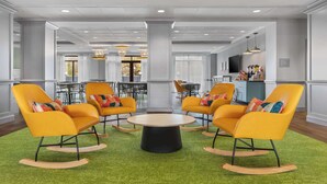 A spacious lobby with a central round table surrounded by yellow rocking chairs, a green carpet, and a modern ceiling design. - Spark by Hilton Charlotte Tyvola I-77 (Charlotte)