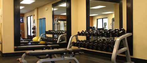 Un gimnasio con equipo de levantamiento de pesas y espejos.