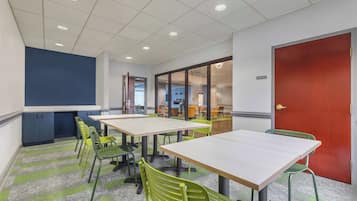 Un salón de conferencias con varias mesas y sillas, techo blanco con iluminación empotrada y una puerta roja.
