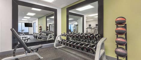 A gym with exercise equipment, mirrors, and a wall-mounted dumbbell rack.