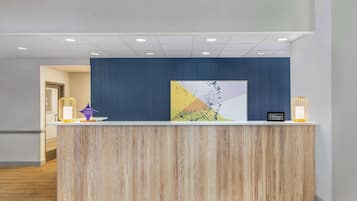 A hotel reception desk with a wooden finish, a blue accent wall, and a modern light fixture.