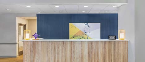 A hotel reception desk with a wooden finish, a blue accent wall, and a modern light fixture.