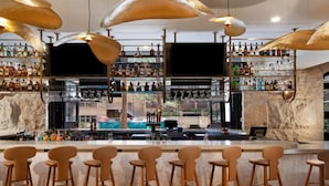A bar area with multiple stools, a television, and shelves stocked with bottles.