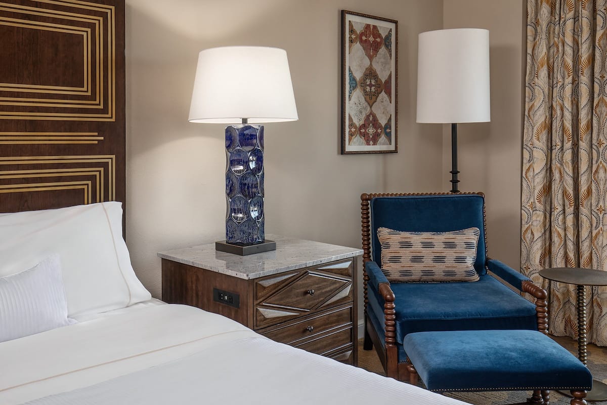 Een hotelkamer met een bed, een nachtkastje, een blauwe fauteuil en twee lampen.