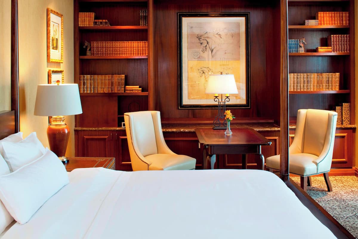 Een hotelkamer met een groot bed, twee fauteuils, een bijzettafeltje en een boekenplank vol boeken.