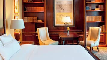 Une chambre d’hôtel avec un grand lit, deux fauteuils, une petite table et une bibliothèque remplie de livres.