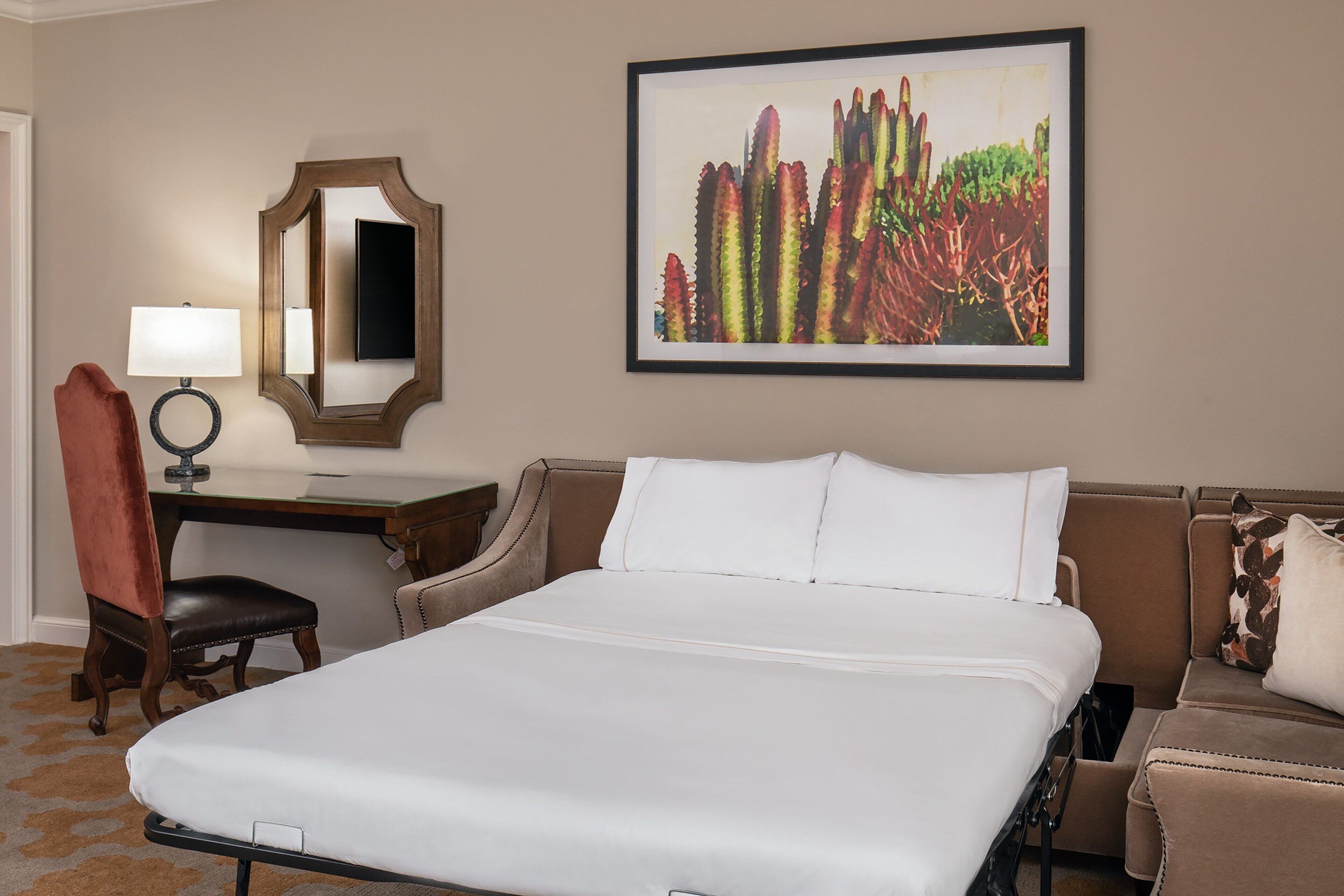 Une chambre d’hôtel avec un grand lit, un bureau avec une lampe, une chaise et un tableau encadré au mur.