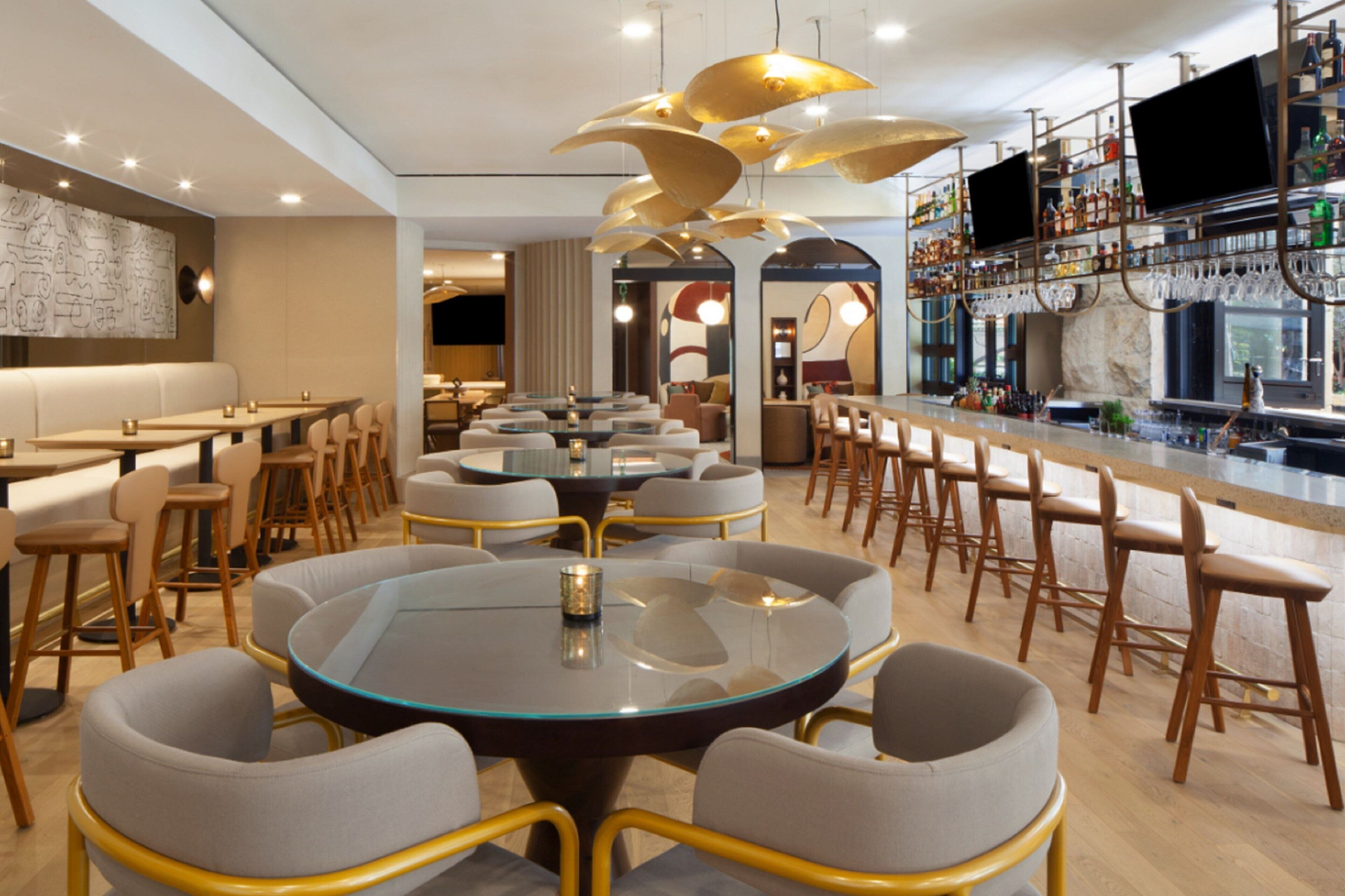 A modern restaurant with round tables, bar seating, and a bar area with shelves of bottles.