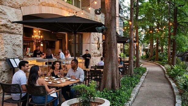 An outdoor dining area with tables and chairs, surrounded by greenery and trees.