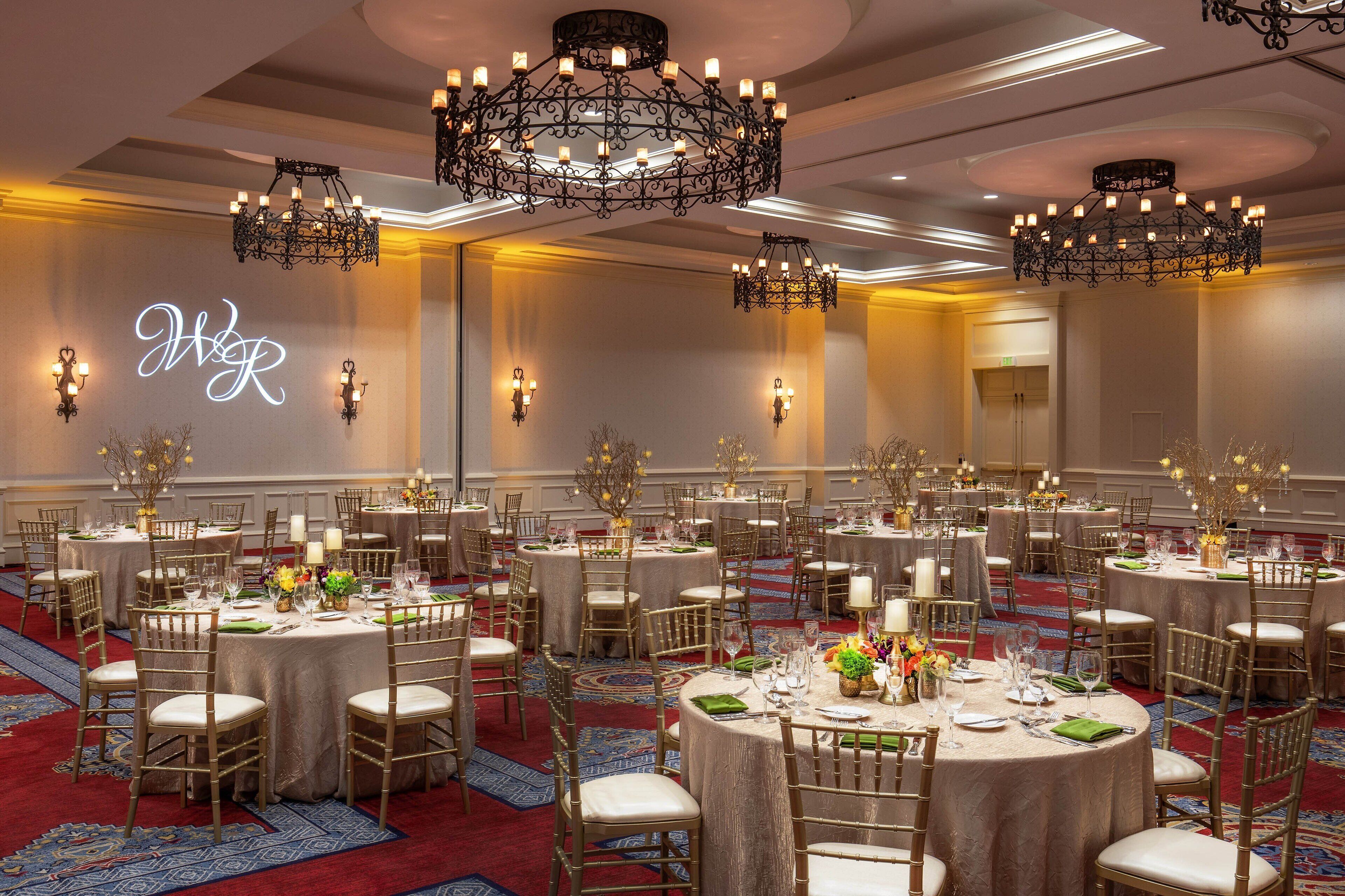 Un salón de banquetes con mesas redondas dispuestas para cenar, candelabros y apliques de pared.