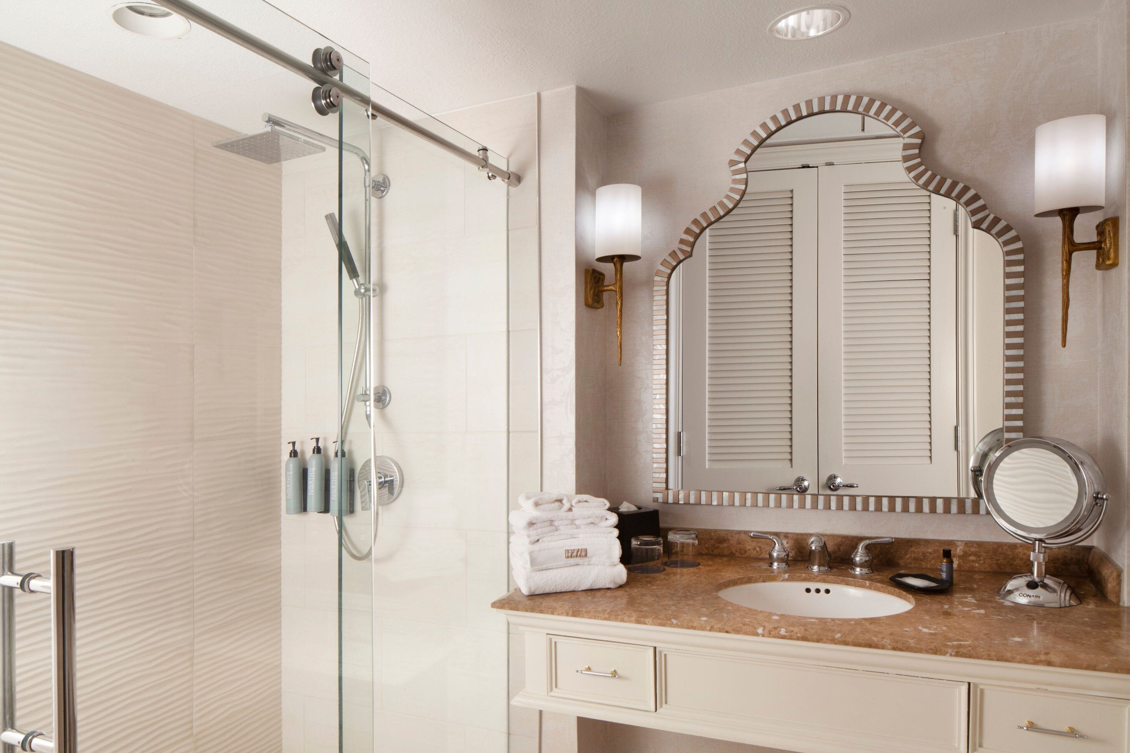 Un baño moderno con cabina de ducha de vidrio, lavabo de mármol y un espejo grande con apliques de pared.