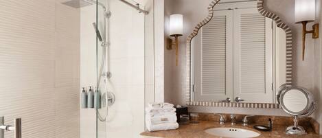 Un baño moderno con cabina de ducha de vidrio, lavabo de mármol y un espejo grande con apliques de pared.