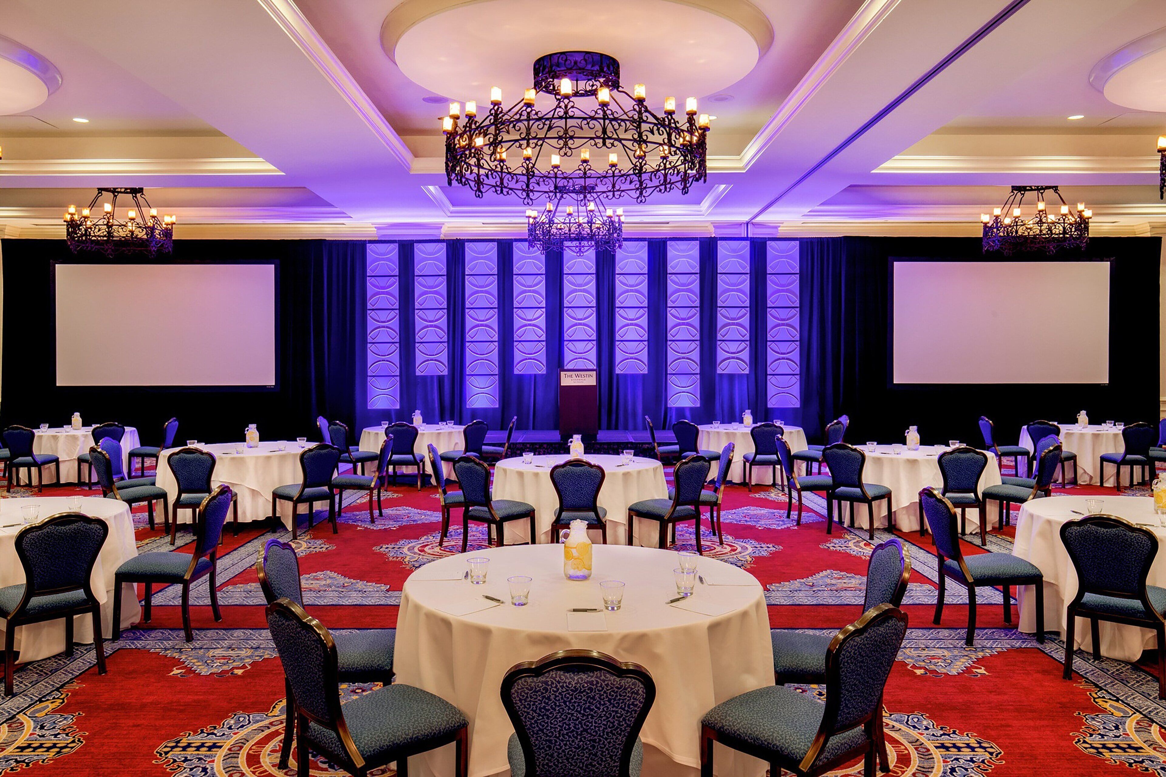 A conference room with round tables, chairs, and a stage with a screen.