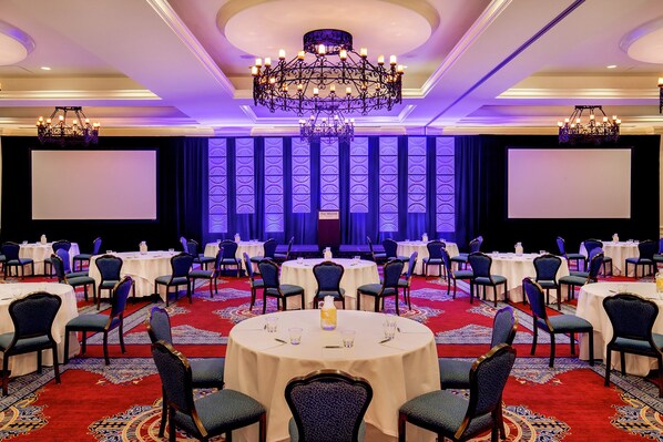 A conference room with round tables, chairs, and a stage with a screen.