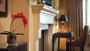Een hotelkamer met een open haard, een bureau met lamp, een stoel en een kamerplant.