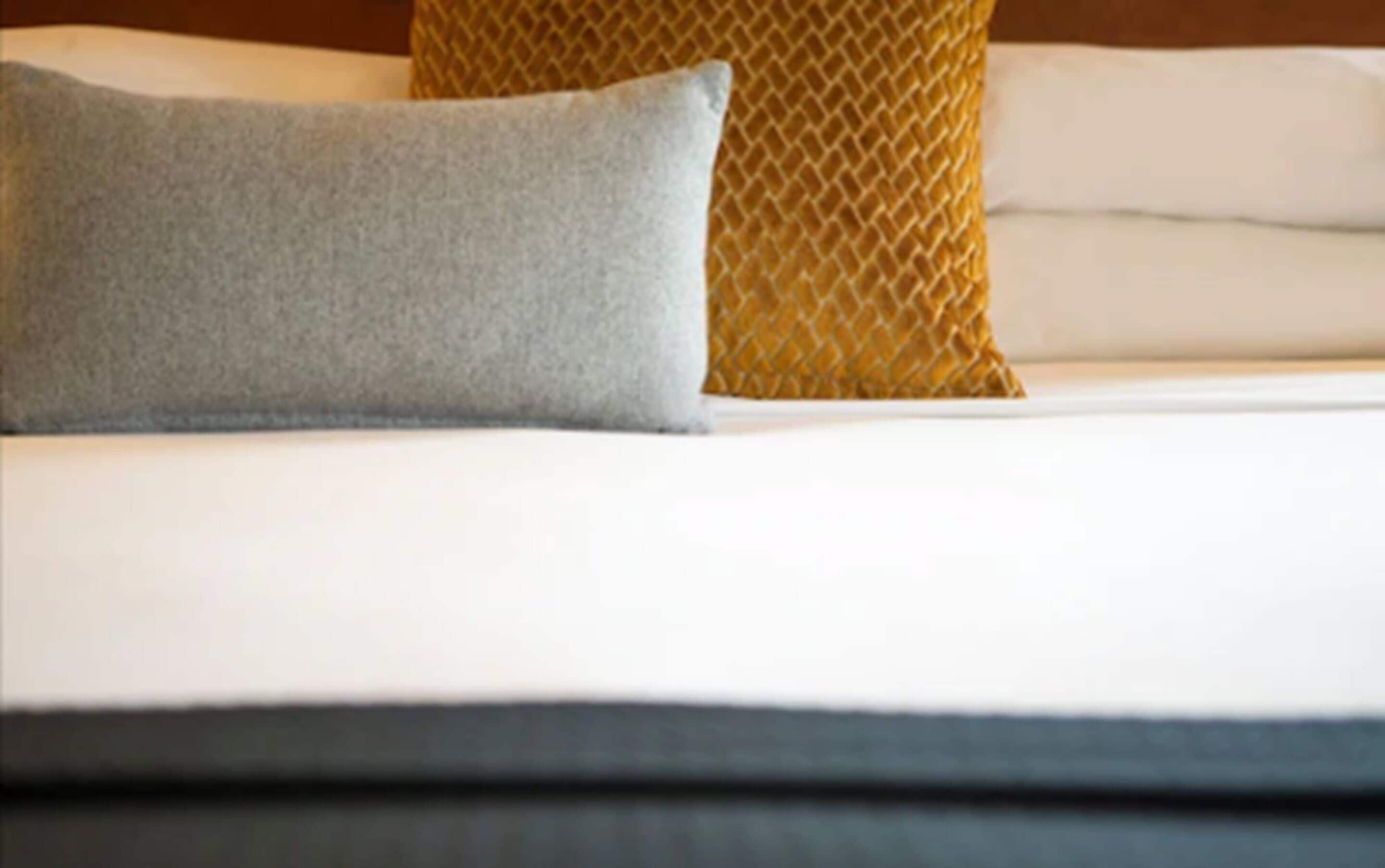 Una cama con un almohadón gris y un cojín estampado.