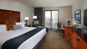 Habitación de hotel con una cama grande, un escritorio con silla, un televisor y vistas al exterior.