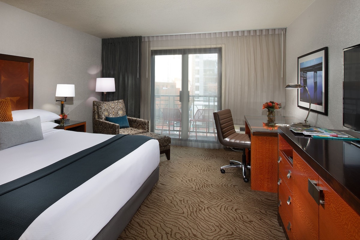 Quarto de hotel com uma cama grande, uma escrivaninha com cadeira, televisão e vista para o exterior.