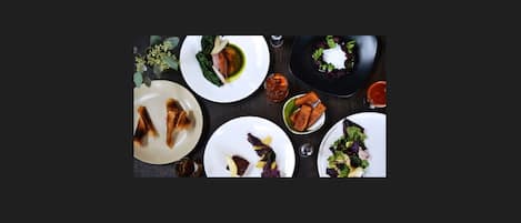 Vue d’ensemble d’une table à manger, avec différents plats, notamment une assiette contenant ce qui semble être un steak, un saladier contenant ce qui pourrait être une salade, et plusieurs autres assiettes avec différents aliments.