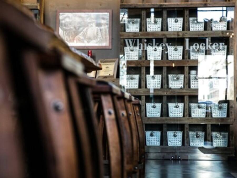 A wooden barrel rack in a rustic setting with a wooden wall and a sign reading "Whiskey Locker."