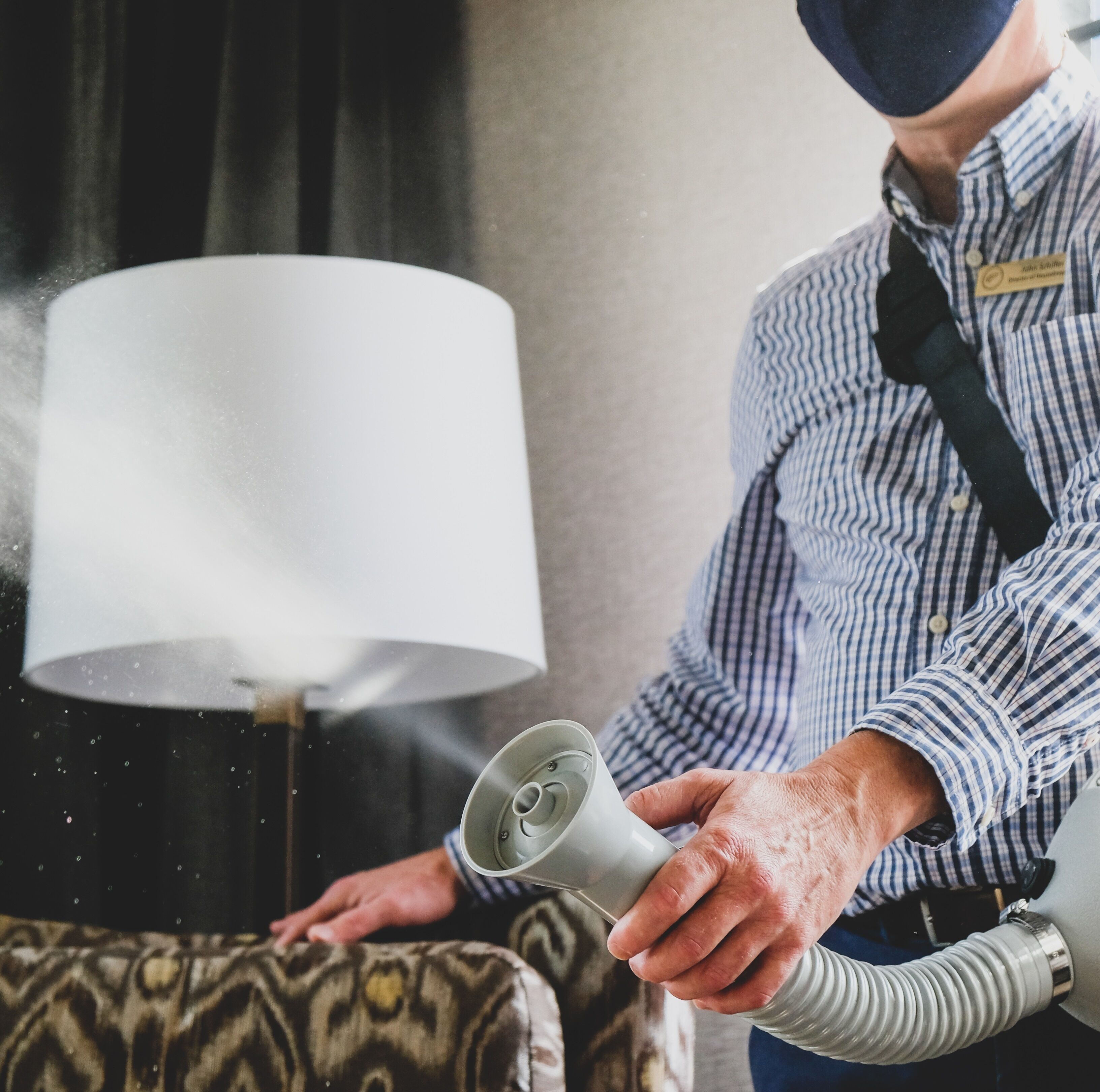 A person holding a device near a lamp, with a patterned sofa in the background.