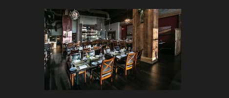A restaurant with multiple tables and chairs, wooden beams, and hanging light fixtures.
