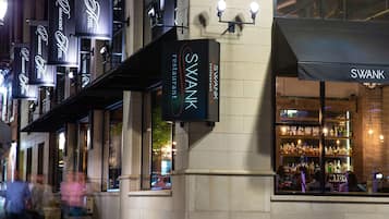 A SWANK restaurant with multiple hanging signs and a well-lit interior visible through the windows.