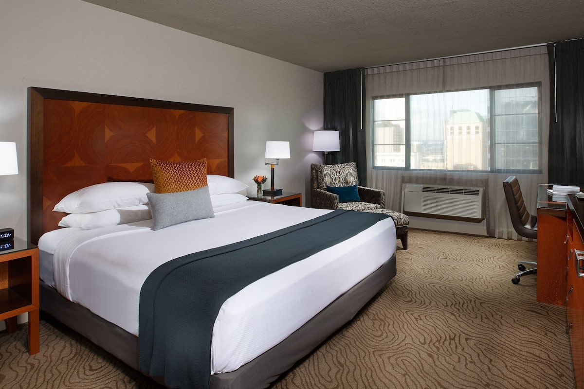 Quarto de hotel com uma cama grande, uma escrivaninha, uma cadeira e uma televisão.