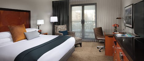 A hotel room with a large bed, a desk, a chair, and a TV.
