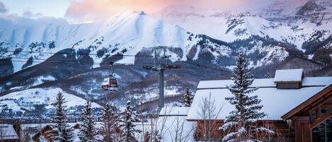 A mountain lodge with a ski lift, snow-covered trees, and a view of snow-capped mountains.