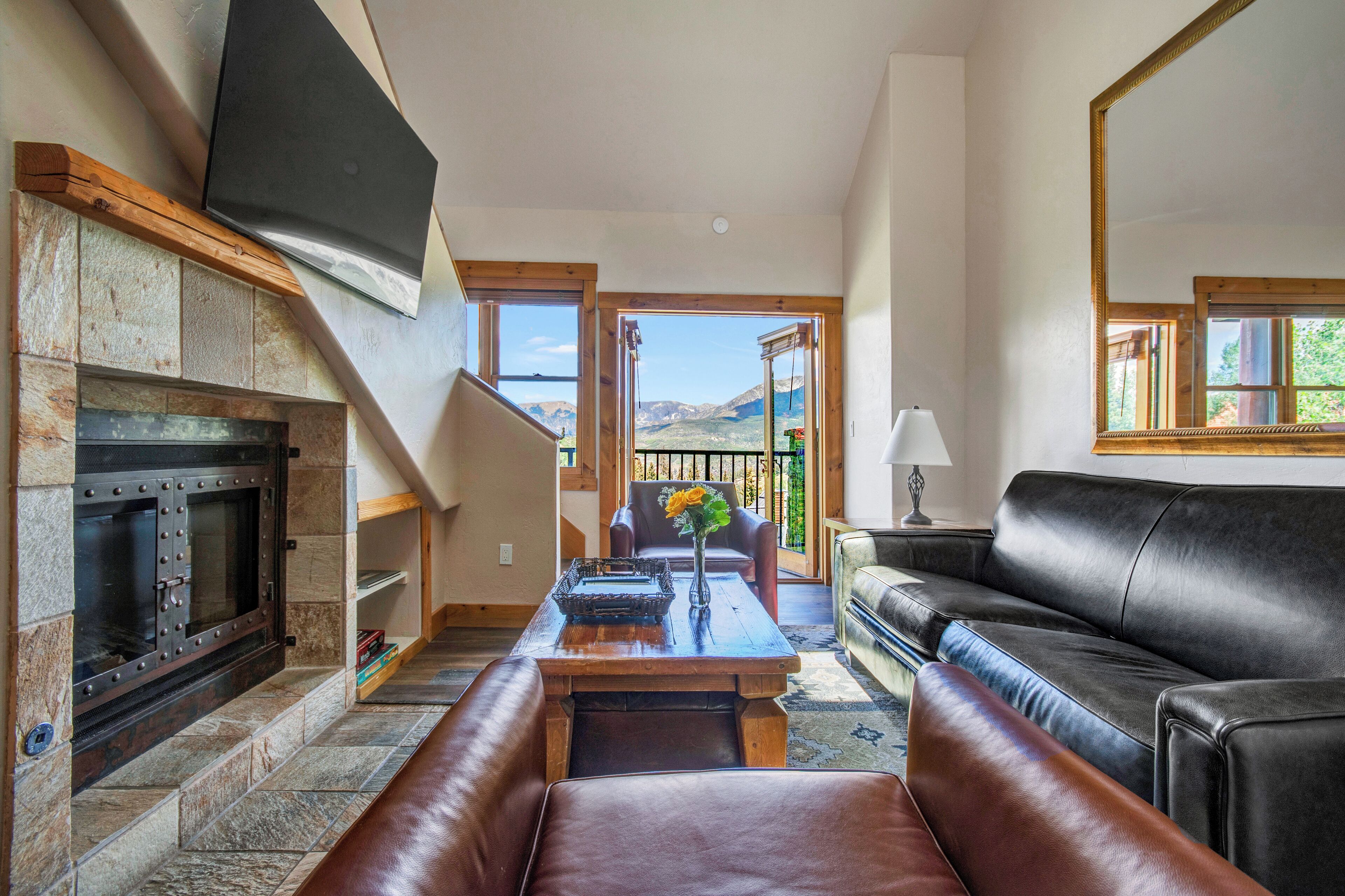A living room with a stone fireplace, leather sofa, and a large TV mounted on the wall.