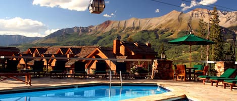 Un espace piscine avec des chaises longues, un téléphérique et une vue sur les montagnes.