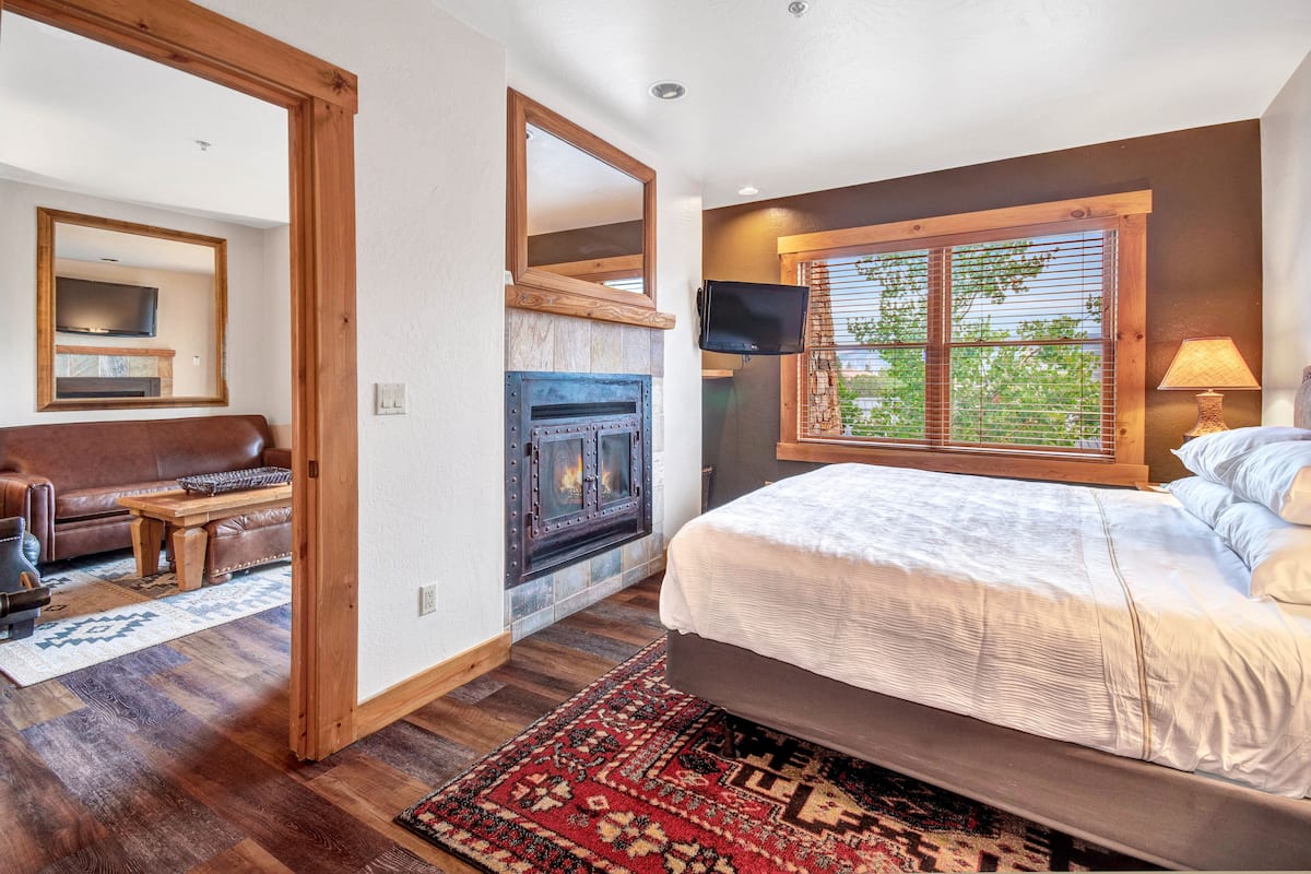 Un dormitorio con cama, chimenea, televisor y ventana con persianas.