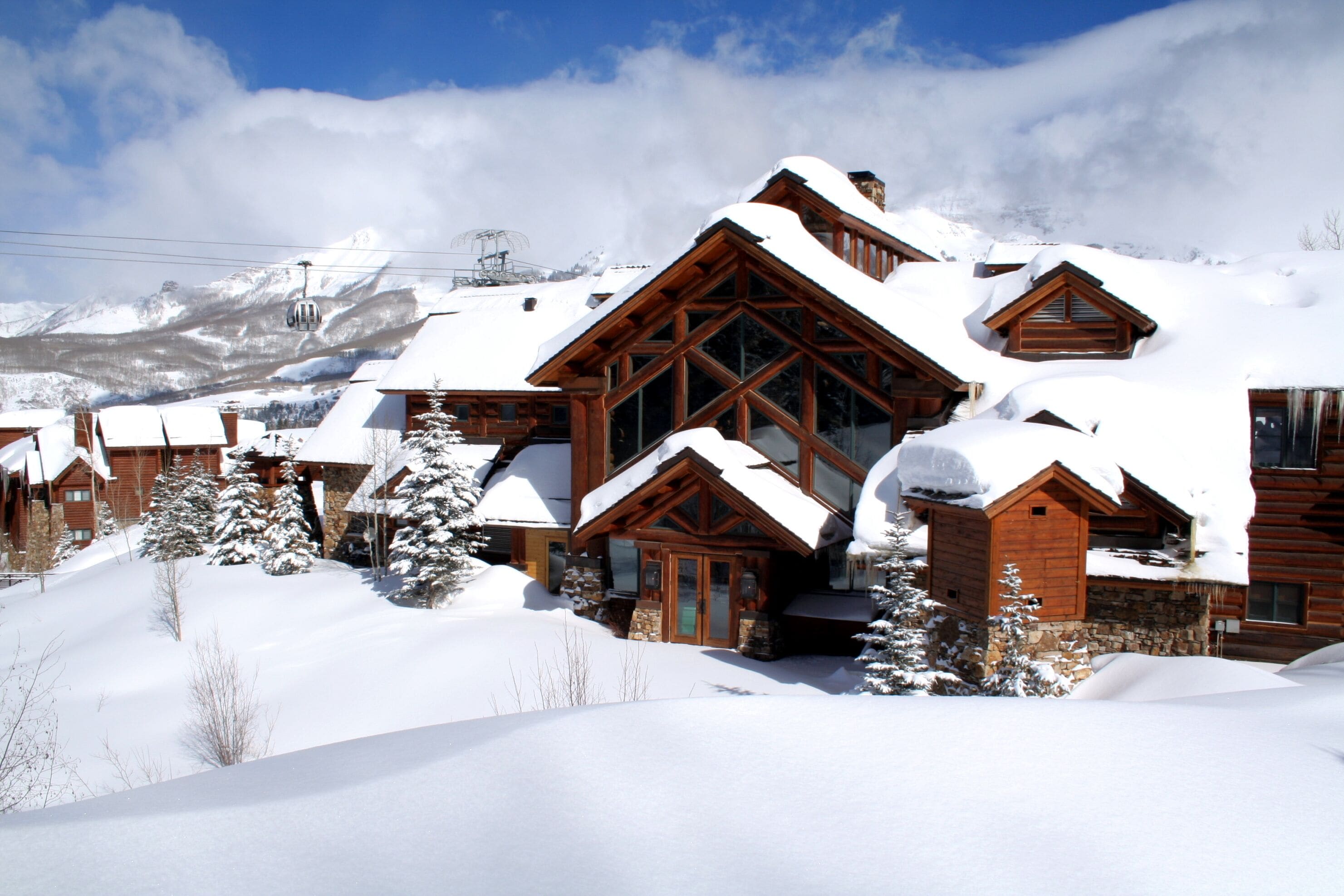A snow-covered lodge with a prominent wooden structure and a mountain backdrop.