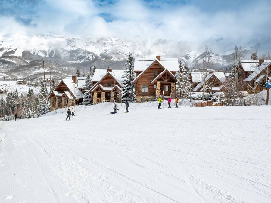 Estância de esqui coberta de neve, com chalés de madeira e montanhas ao fundo.